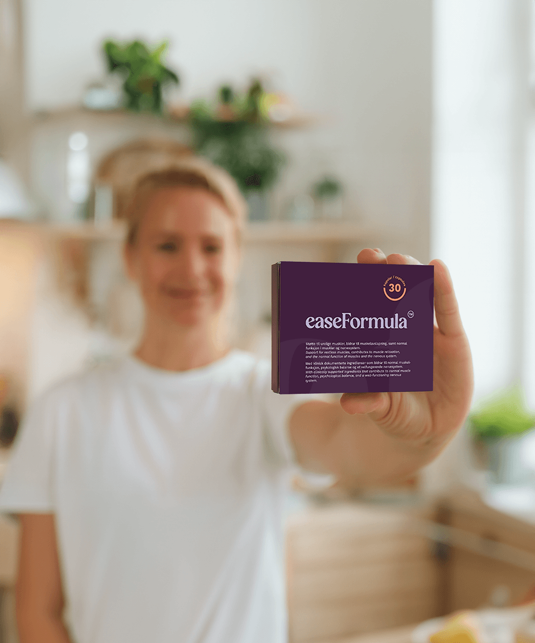 Kvinne holder frem en pakke EaseFormula – kosttilskudd med magnesium, silkepion og L-teanin, 30 kapsler